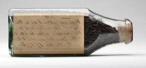 shriveled brown tea leaves sit inside a glass bottle 这是 closed up with a cork; cursive handwriting in brown ink on a yellowed paper is inside the bottle
